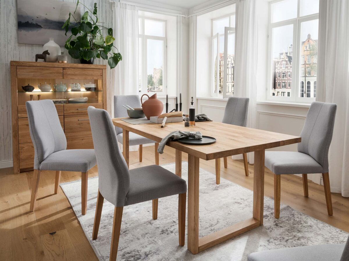 Drewniany stół i szare krzesła w skandynawskiej jadalni z dużymi oknami