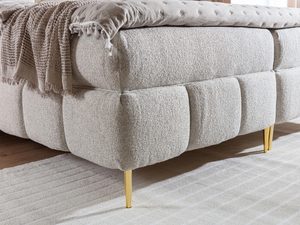 Miniaturka 11 - Przybliżenie na beżowa tkaninę łóżka tapicerowanego oraz złote nogi