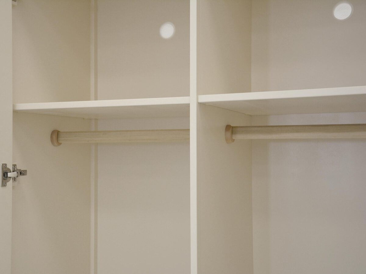 Wnętrze szafy drewnianej z drążkami na ubrania w kolorze ecru