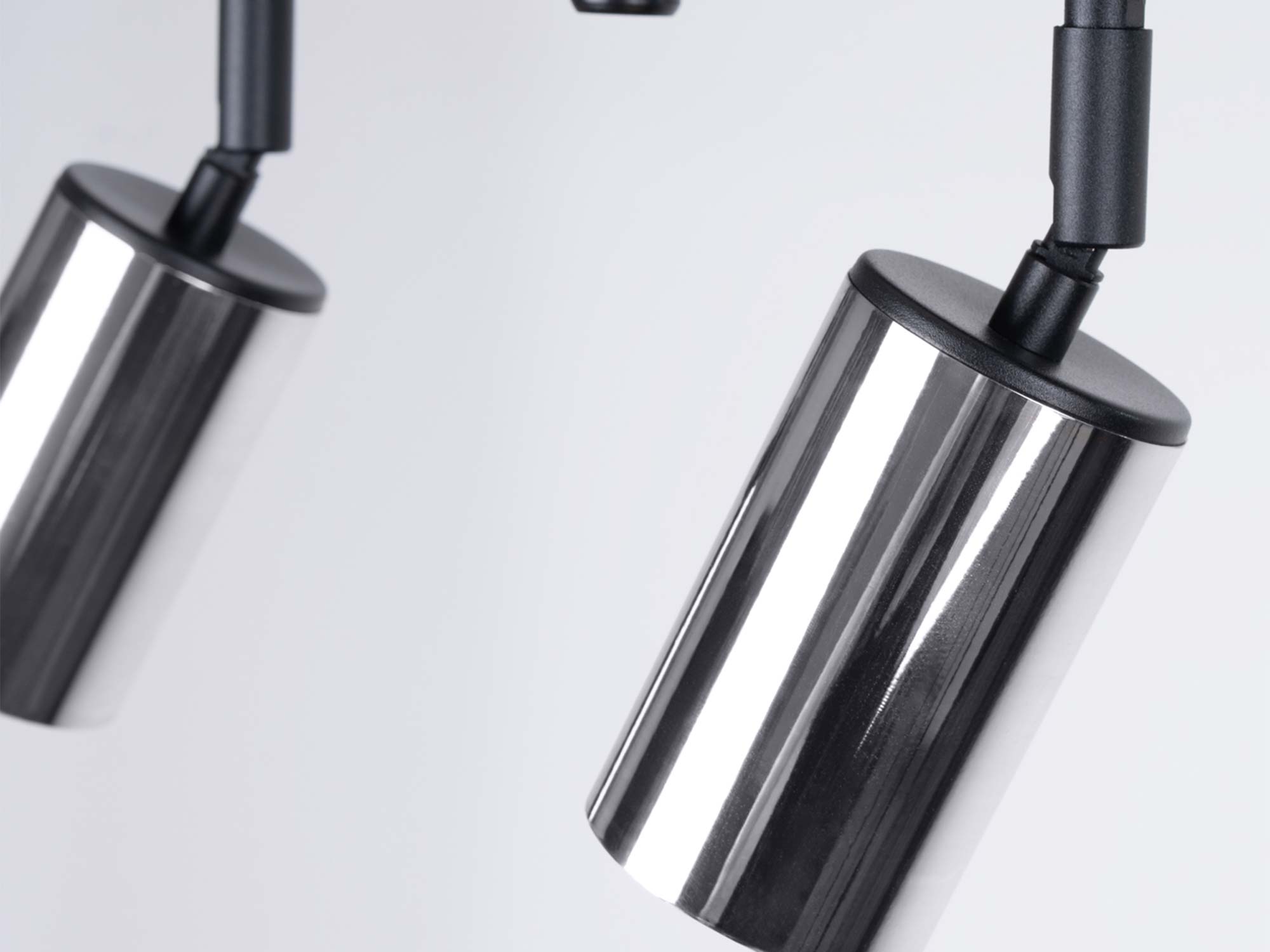 Detal dwóch chromowanych reflektorów cylindrycznych plafonu z czarnymi mocowaniami zbliżenie Detal dwóch chromowanych reflektorów cylindrycznych plafonu z czarnymi mocowaniami zbliżenie