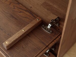 Miniaturka 15 - Detal klapy komody tabacco z drewnianym uchwytem i zawiasem