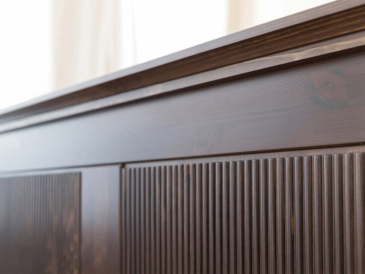Detal górnego gzymsu mebla drewnianego ciemnobrązowego z ryflowanymi panelami