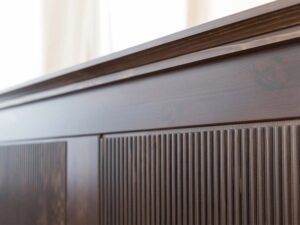 Miniaturka 8 - Detal górnego gzymsu mebla drewnianego ciemnobrązowego z ryflowanymi panelami