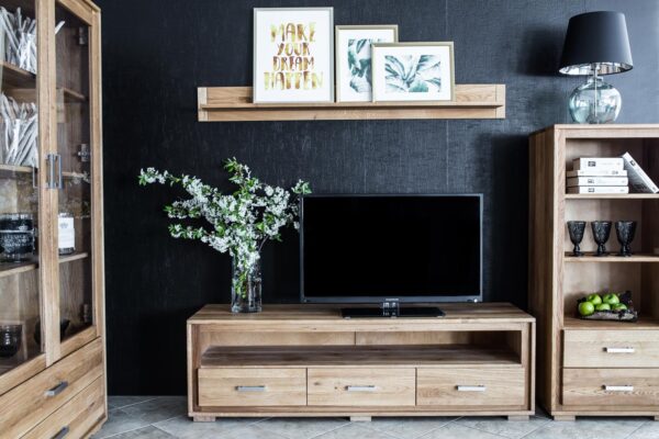 Salon z meblami dębowymi szafką RTV witryną i regałem na ciemnej ścianie
