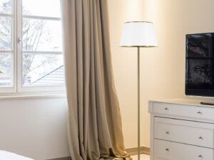 Miniaturka 1 - Lampa podłogowa Amevio z jasnym abażurem ustawiona w sypialni obok komody
