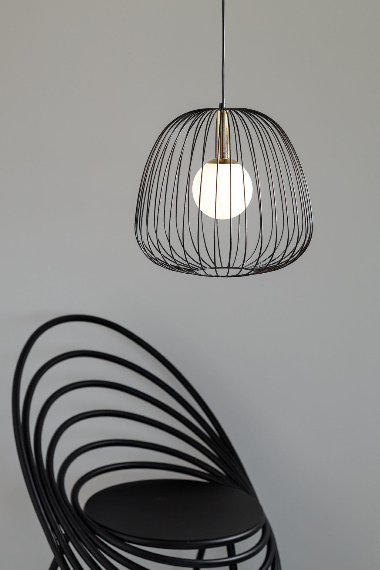 Lampa Bell 1 M czarno-złota nad designerskim czarnym krzesłem, ujęcie aranżacyjne