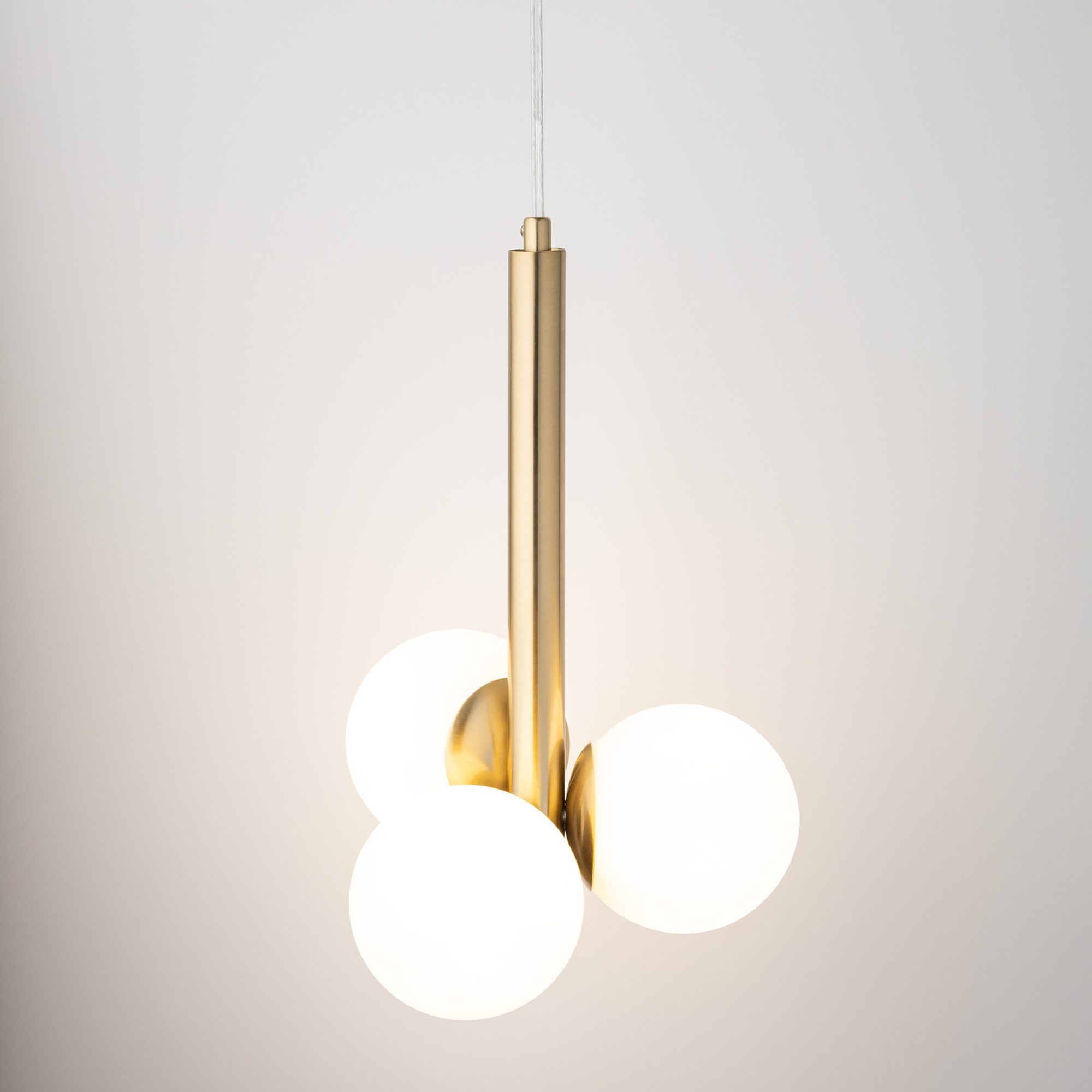 Lampa wisząca Perla Lux 3, białe szklane kule rozświetlone wokół złotego pionowego korpusu.