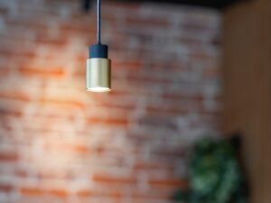Miniaturka 5 - Czarno-złota lampa Puri 2.0 Tube zawieszona w aranżacji przy ceglanej ścianie