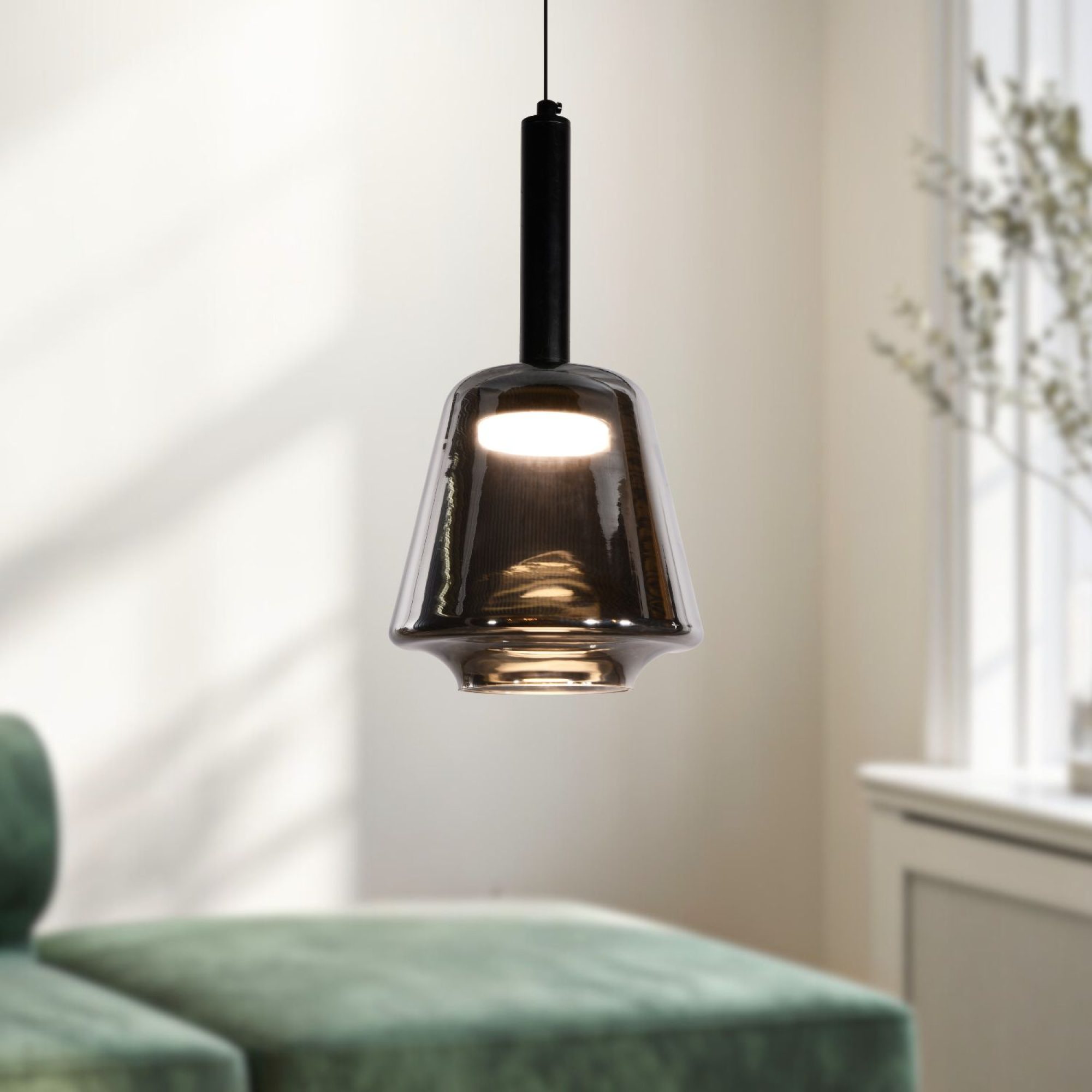 Lampa wisząca Rominia z dymionym szklanym kloszem i włączonym światłem nad sofą