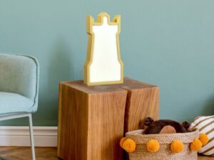 Miniaturka 3 - Złota lampka LED w kształcie wieży zamkowej ustawiona na drewnianym stoliku w pokoju
