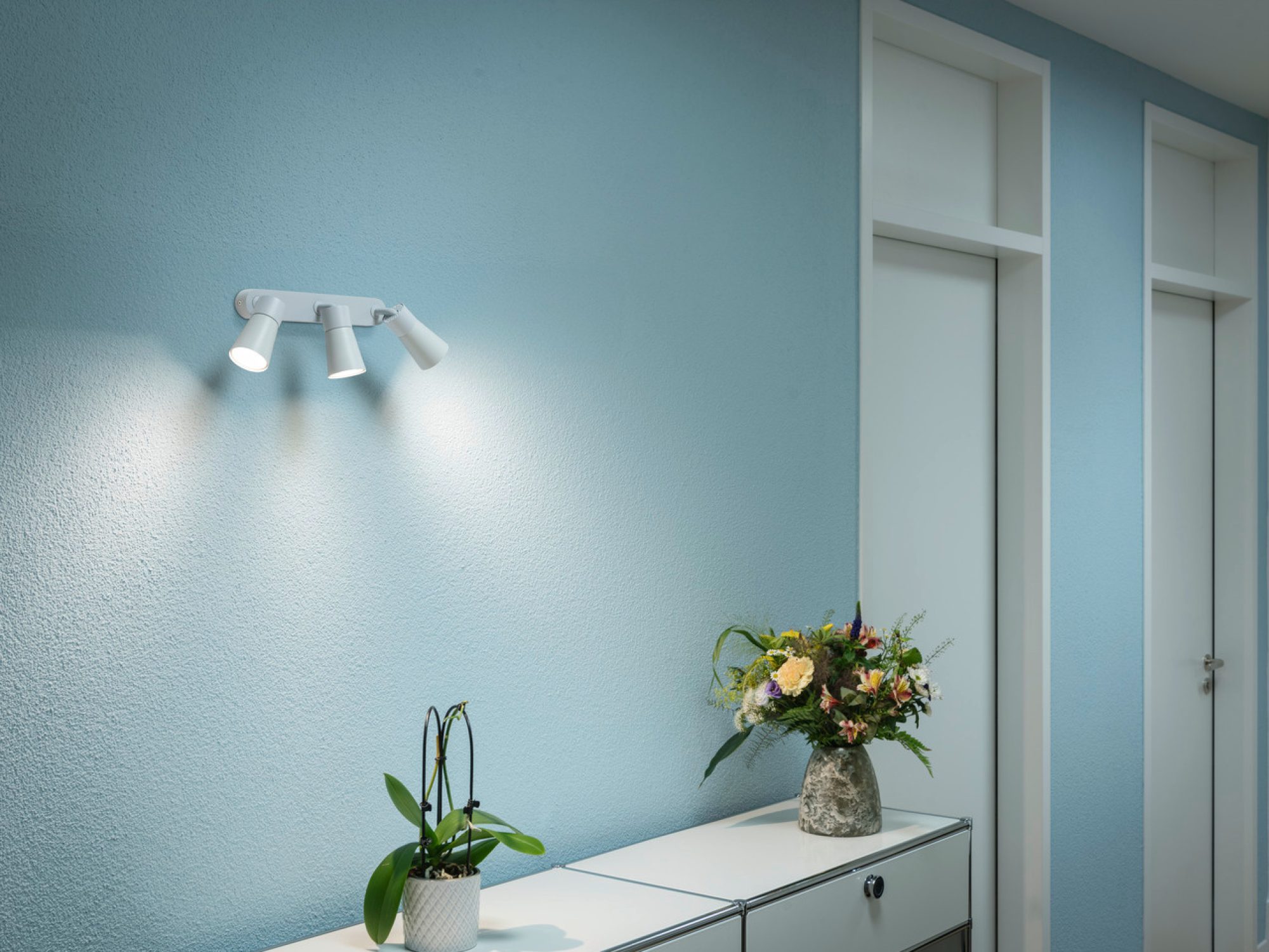 Biała lampa Puri 2.0 Dome na niebieskiej ścianie nad komodą