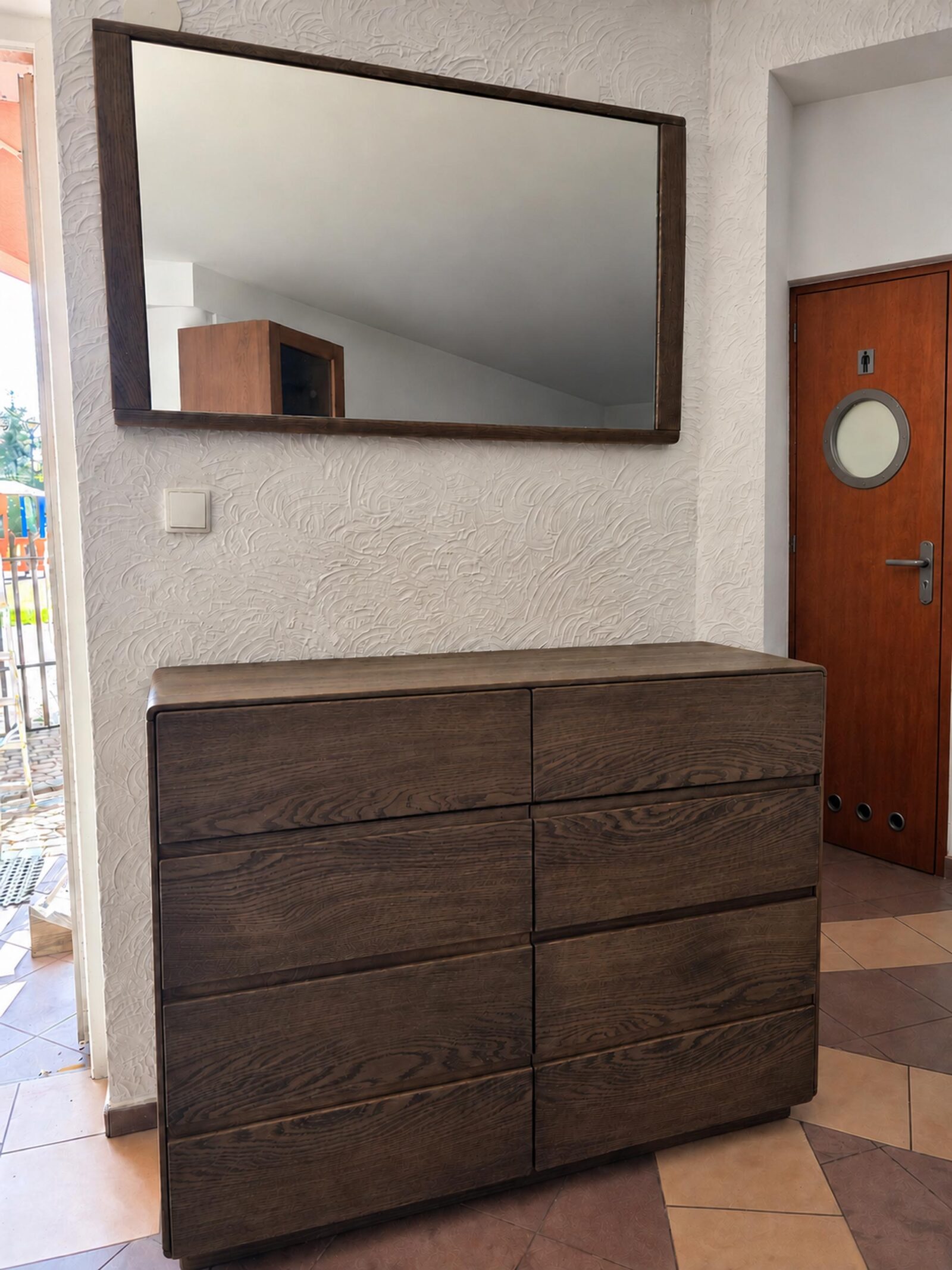 Komoda z ciemnego dębu z ośmioma szufladami i lustro w drewnianej ramie w salonie IGA Meble w Leżajsku